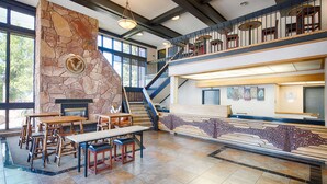 Un hall d’entrée spacieux avec une cheminée en pierre, des tables et des chaises en bois, un escalier et des œuvres d’art accrochées aux murs.