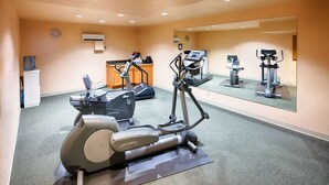 Une salle de sport équipée de machines de cardio, d’un distributeur d’eau et d’un miroir qui reflète l’équipement.