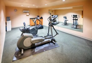 A gym with cardio machines, a water dispenser, and a mirror reflecting the equipment.