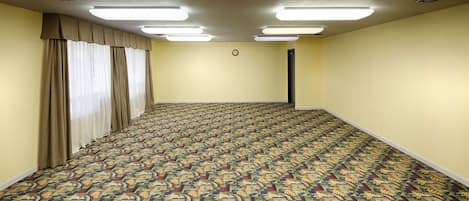 Uma sala de conferências com carpete estampado, paredes bege e um grande janelão com cortinas.