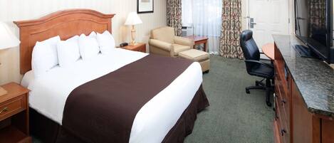 A hotel room with a large bed, a desk with a television, a chair, and a small table.