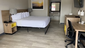 Ein Hotelzimmer mit Bett, Nachttischlampen, einem Schreibtisch mit Stuhl, einem Fernseher und einem durch eine offene Tür einsehbaren Badezimmer.