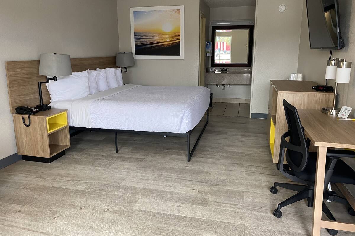 A hotel room with a bed, bedside lamps, a desk with a chair, a television, and a bathroom visible through an open door.