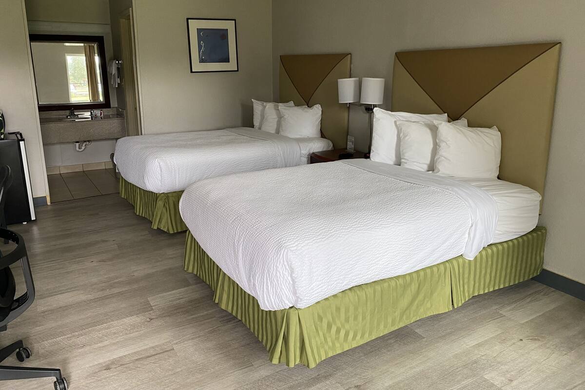 A hotel room with two beds, a bathroom, and a desk.
