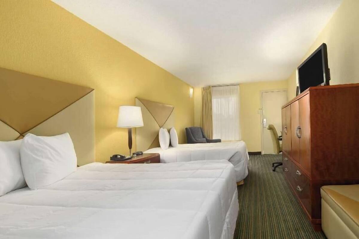 A hotel room with two beds, a desk, a chair, a television, and a wardrobe.