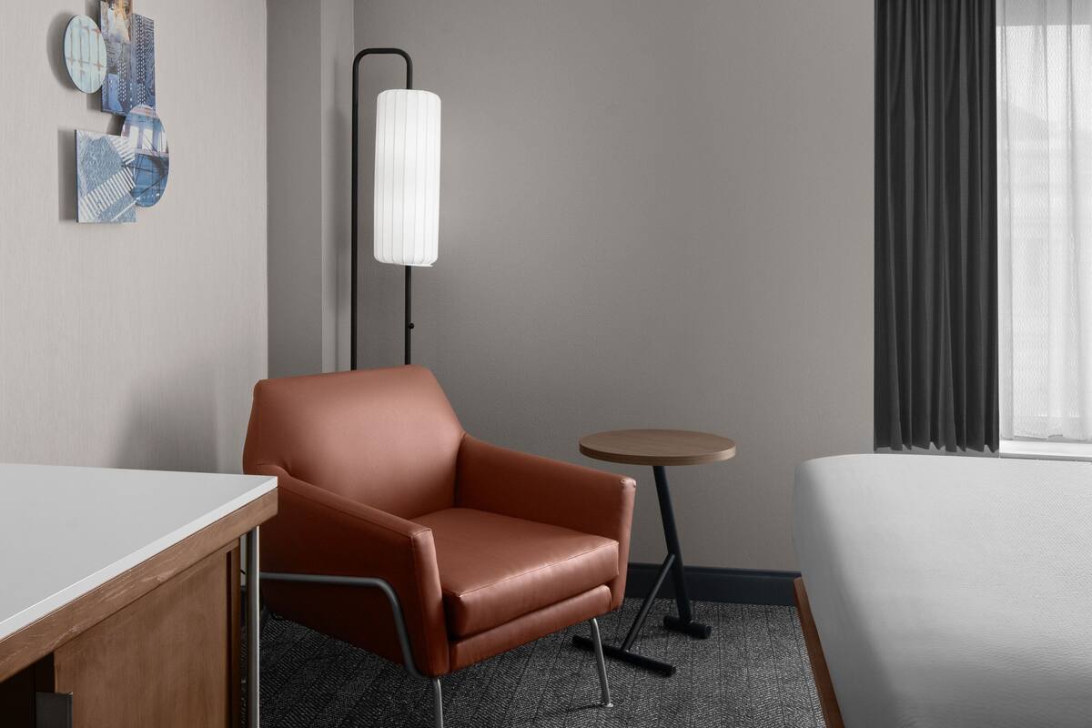 A hotel room with a single bed, a desk, a chair, a small round table, and a floor lamp.