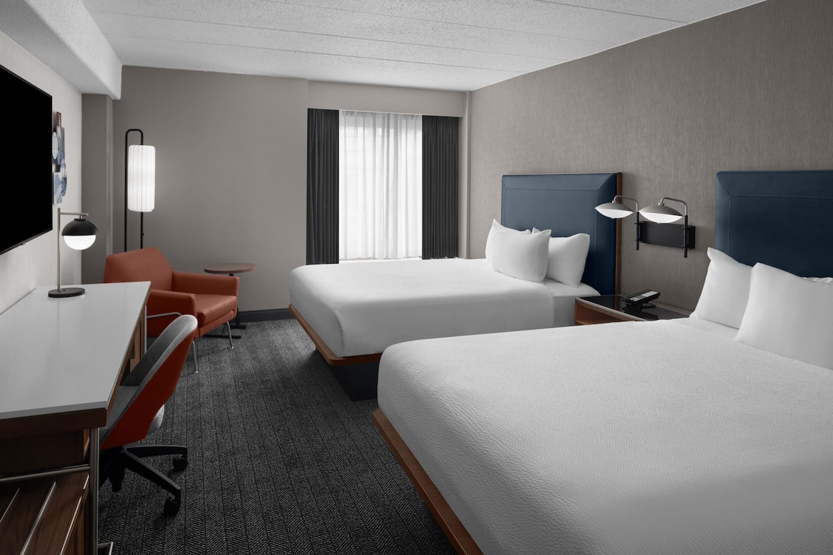 Een hotelkamer met twee bedden, een bureau, een stoel, een lamp en een raam met gordijnen.