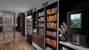 A modern hotel lobby with a coffee machine, snack shelves, and a refrigerator.