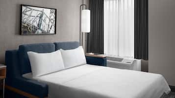 A hotel room with a bed, a nightstand, a lamp, a window with curtains, and a framed picture on the wall.