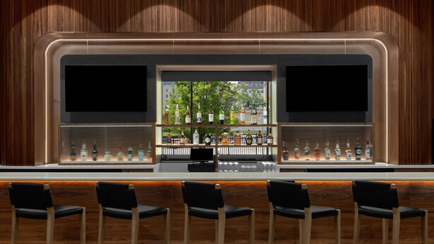 A bar area with a wooden backdrop, a glass display case with bottles, and four black bar stools.