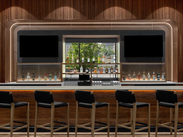A bar area with a wooden backdrop, a glass display case with bottles, and four black bar stools.