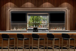 Un espace bar avec un fond en bois, une vitrine en verre contenant des bouteilles et quatre tabourets de bar noirs.