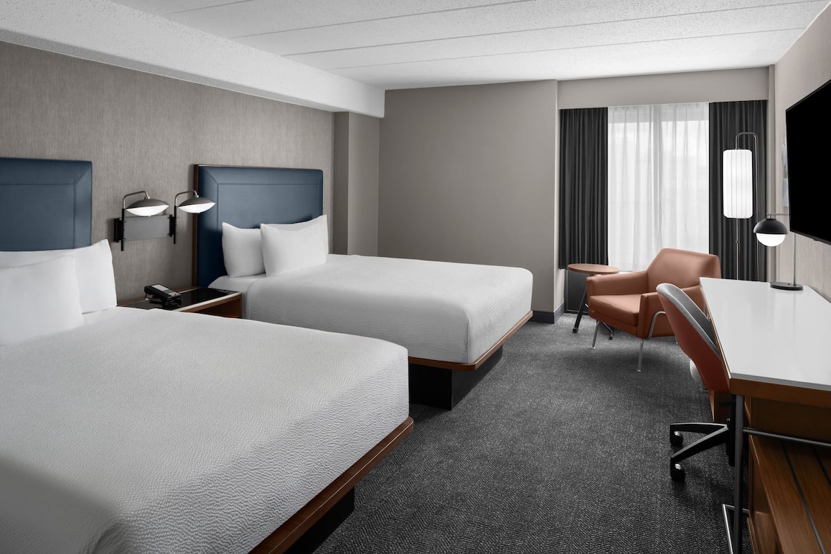 Hotelkamer met twee bedden, een bureau, een stoel, een televisie en een raam met gordijnen.