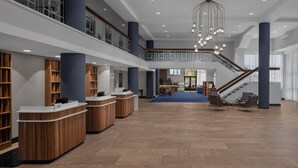 A spacious lobby with a central staircase, wooden reception desks, and a seating area.
