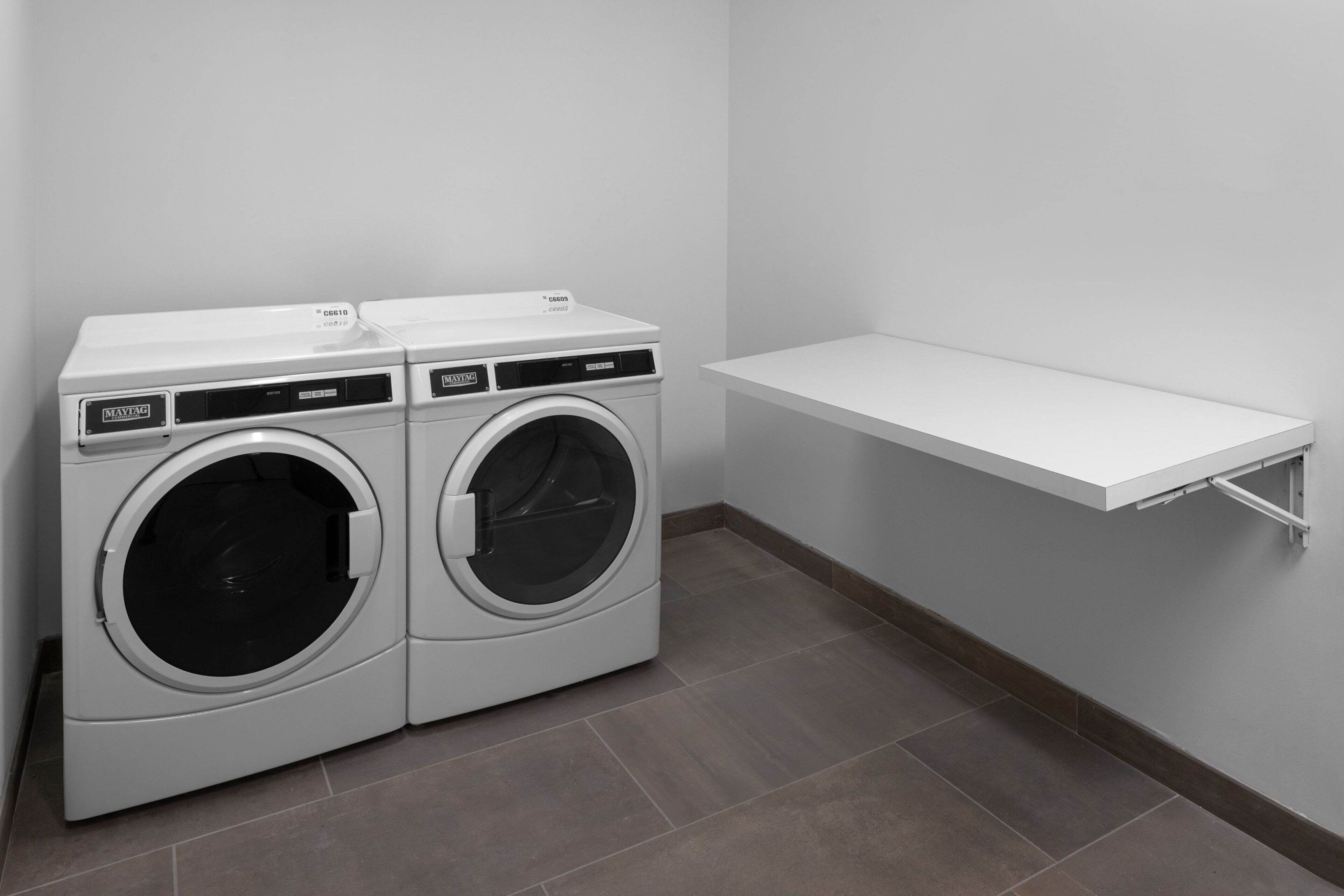 A laundry area with two front-loading washing machines and a white shelf.