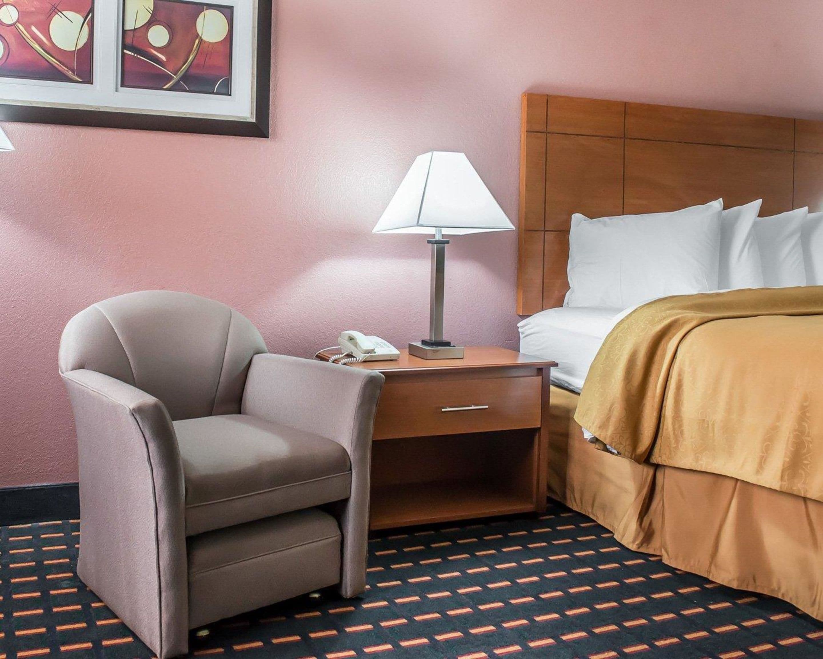 A hotel room with a bed, a desk with a lamp, a chair, and a phone.