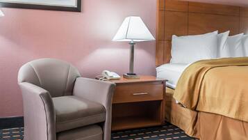 A hotel room with a bed, a desk with a lamp, a chair, and a phone.