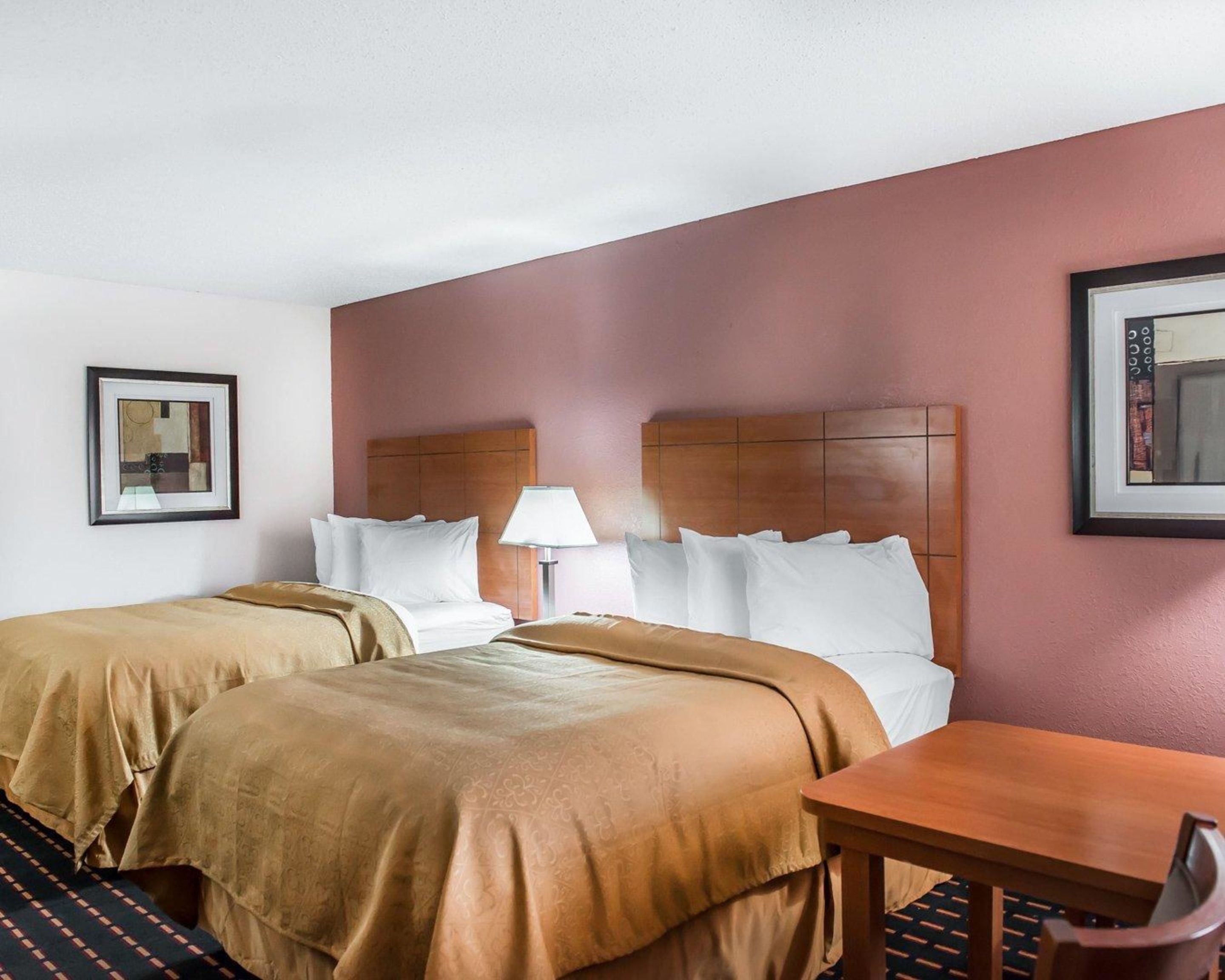 A hotel room with two beds, a wooden headboard, a table, and a lamp.