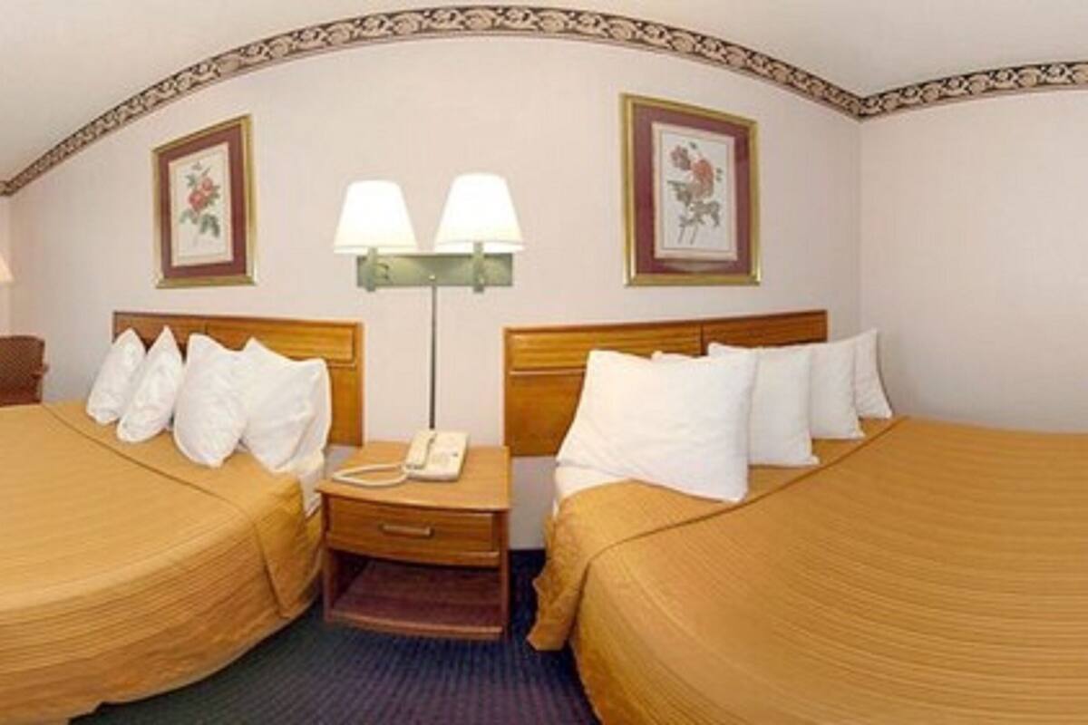 A hotel room with two beds, a desk, a chair, and a lamp.