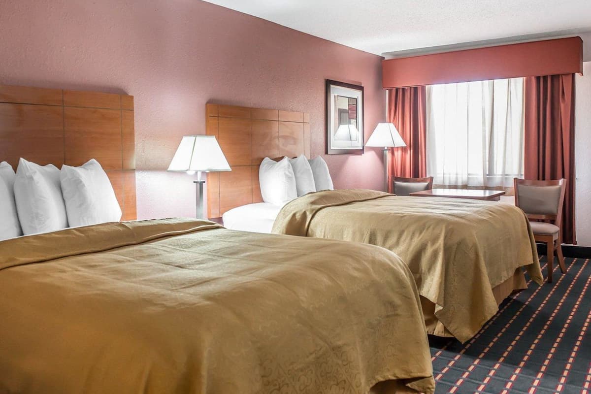 A hotel room with two beds, a desk, a chair, and a window with curtains.