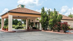 A hotel with a covered entrance, a tiled roof, and a landscaped garden with trees and shrubs. - Quality Inn Marianna South (Marianna)
