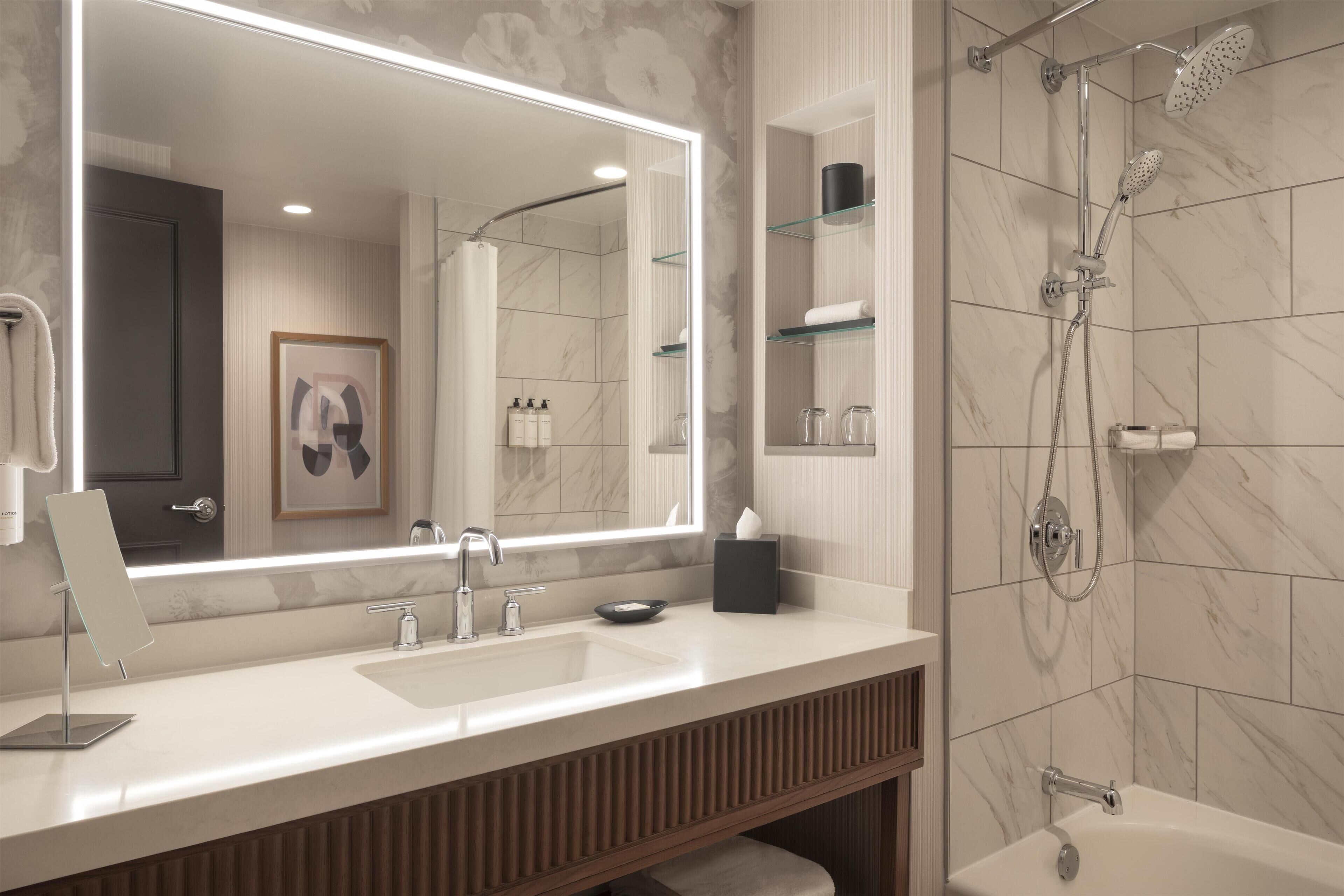A modern bathroom with a large mirror, a sink, a shower, and a toilet.