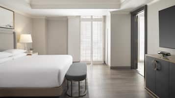 Una habitación de hotel moderna con una cama grande, un banco, una mesita de noche con lámpara, un armario y un ventanal con persianas.
