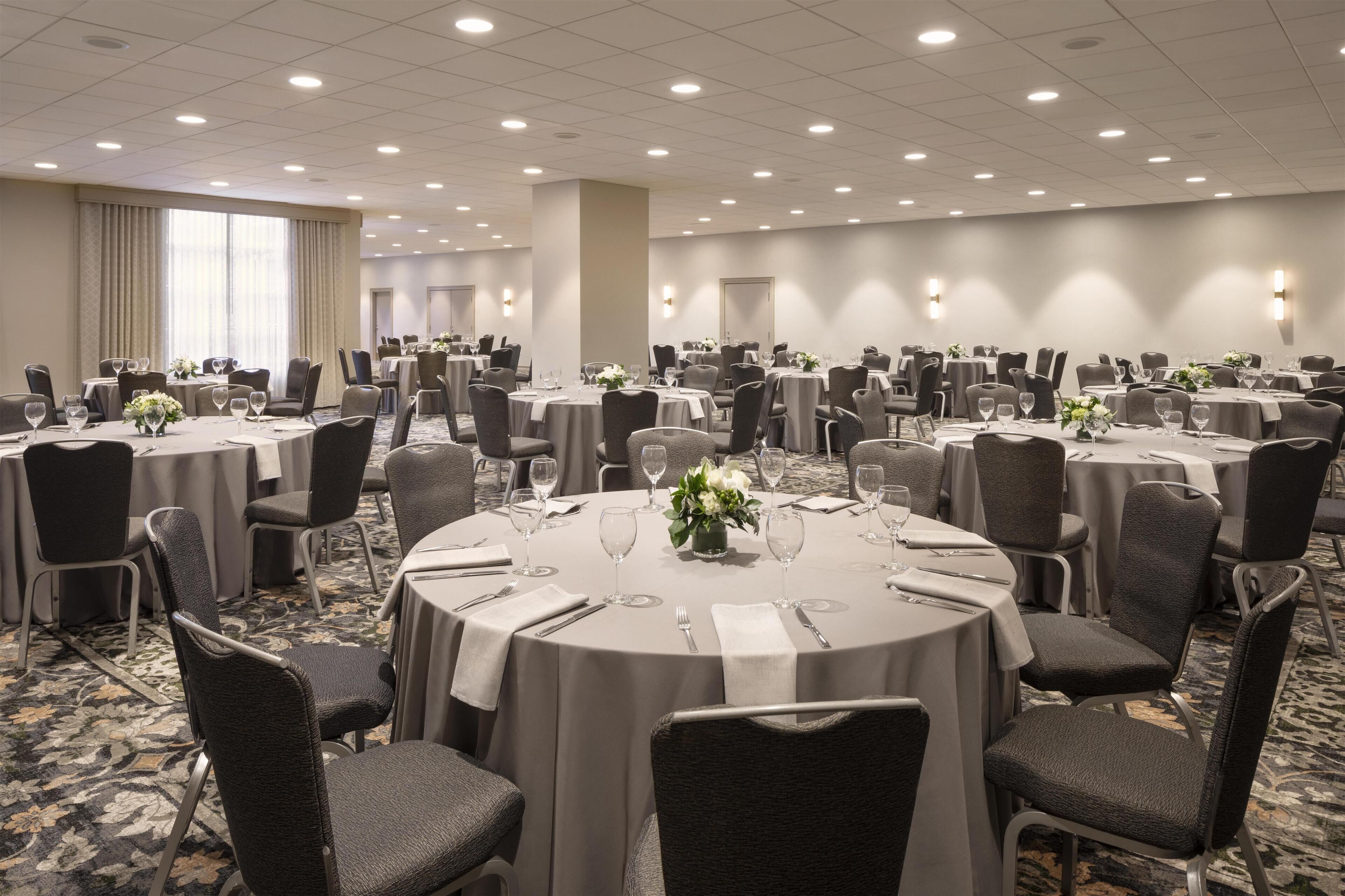 A large banquet hall with round tables, each set with chairs, glasses, and a centerpiece.