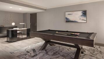 A modern pool table in a room with a neutral color scheme, a desk, and a framed abstract painting on the wall.