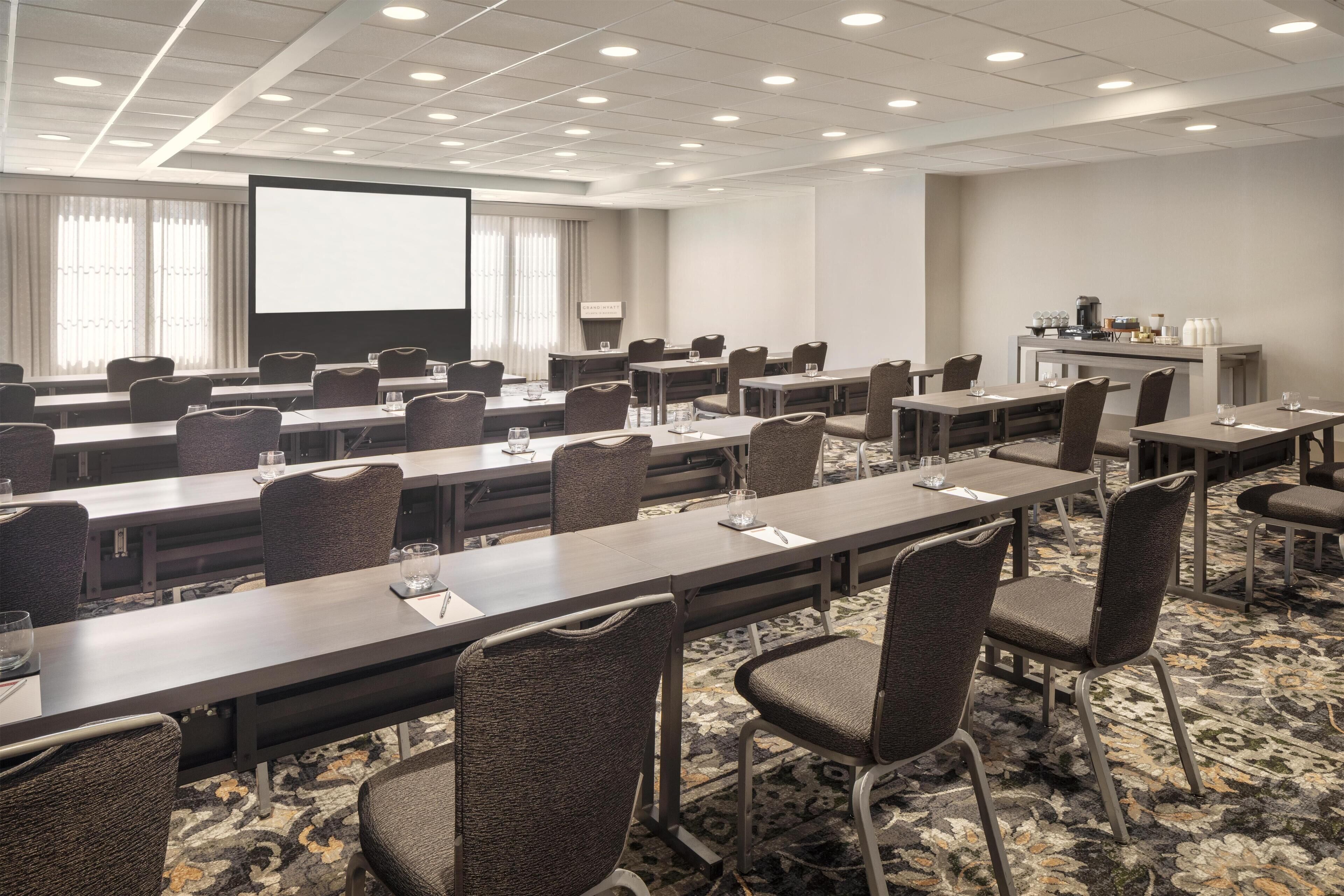 A conference room with multiple tables and chairs, a projector screen, and a coffee station.