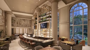 A spacious bar area with a high ceiling, large windows, and a variety of seating arrangements including bar stools and tables.