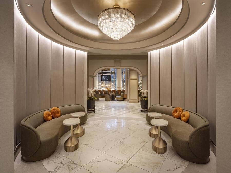 A luxurious lobby with a grand chandelier, plush seating, and a view of the bar area.