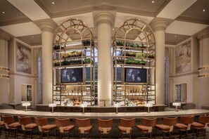 A bar area with multiple seating arrangements, a central bar counter, and shelves with plants and bottles.