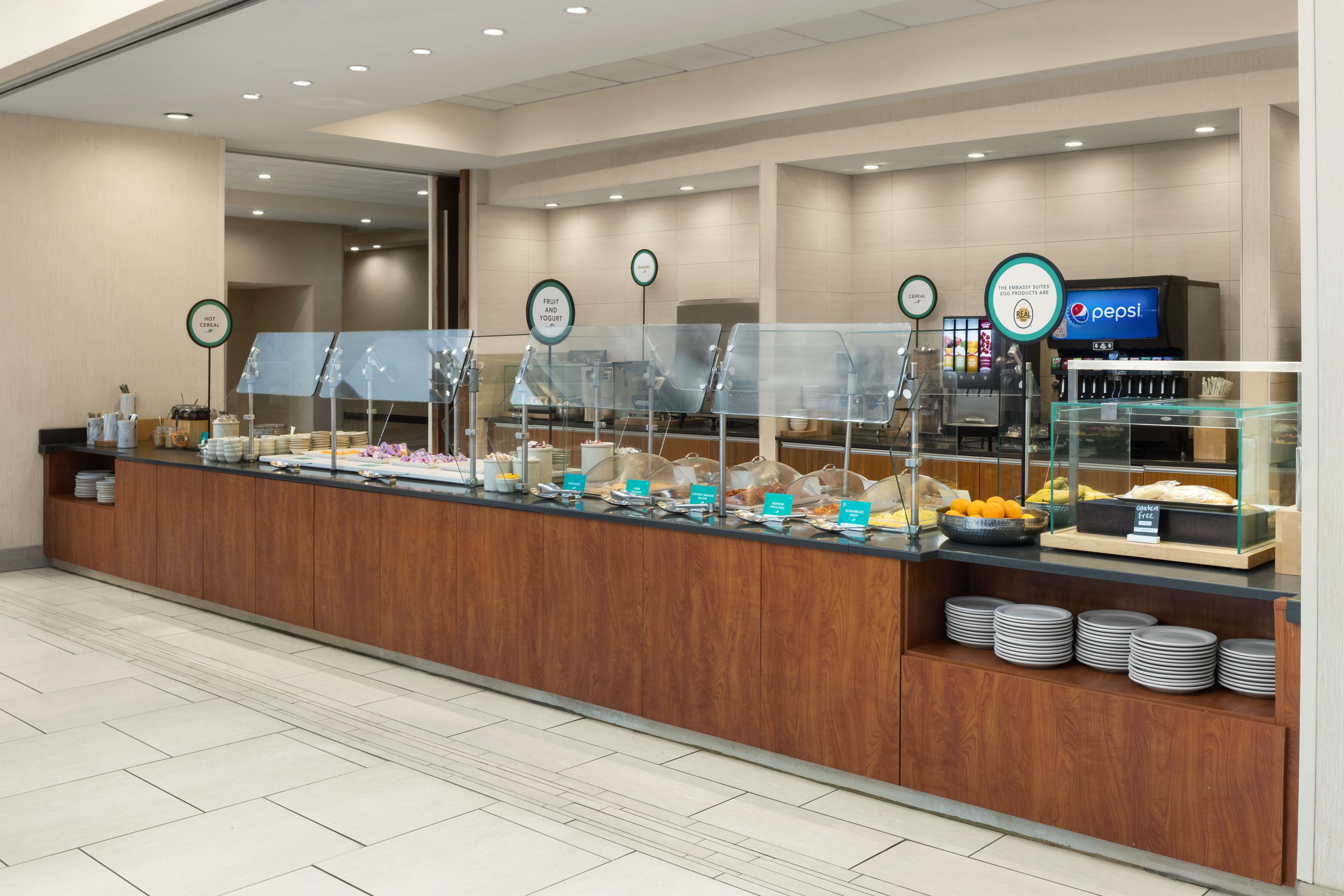 A buffet area with various food stations, including a fruit and yogurt section, and a Pepsi refrigerator.