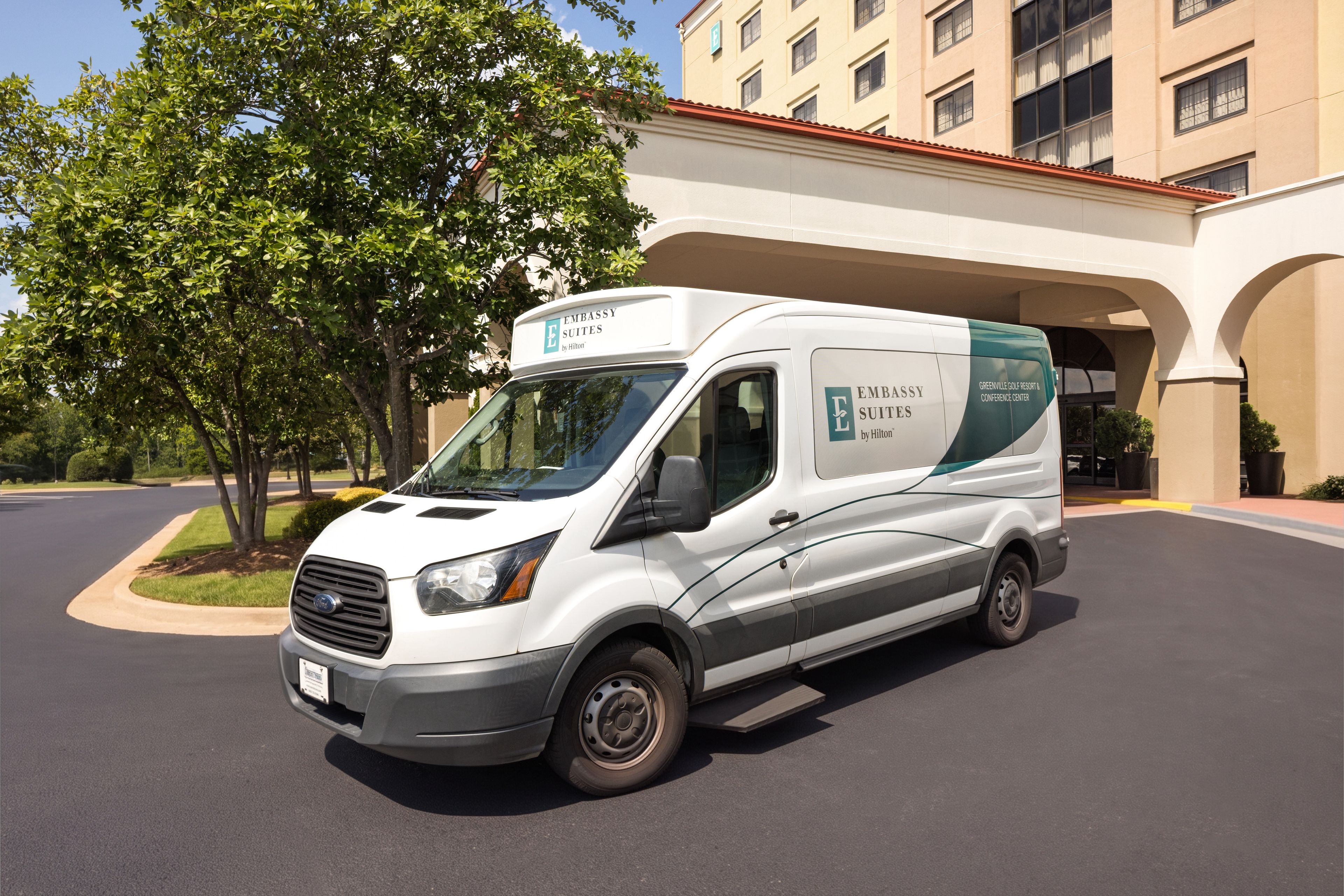 A white van parked in front of a building with a sign that reads 'Embassy Suites by Hilton.'