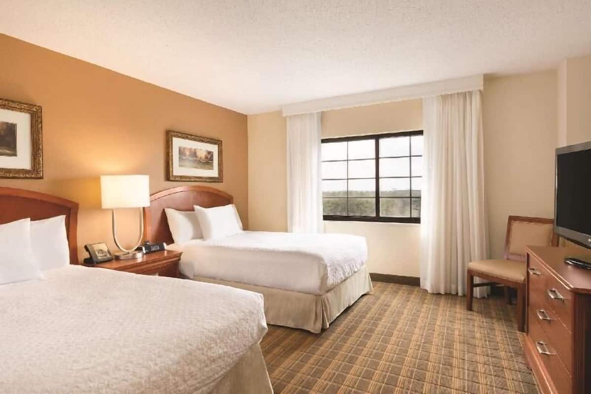 Une chambre d’hôtel avec deux lits, une télévision, un bureau et une fenêtre avec des rideaux.