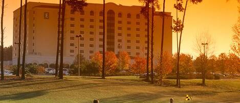 A golf course with players, a large building in the background, and trees with autumn foliage.
