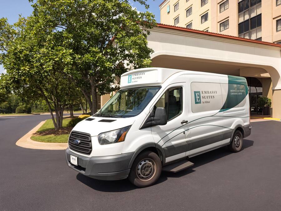 A white van with 'Embassy Suites by Hilton' branding parked in front of a building with a red roof.