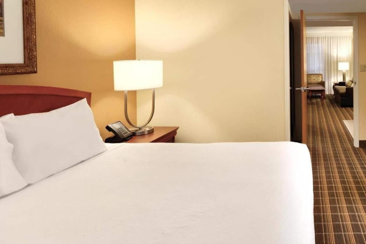 A hotel room with a bed, a bedside lamp, a telephone, and a view of the hallway.