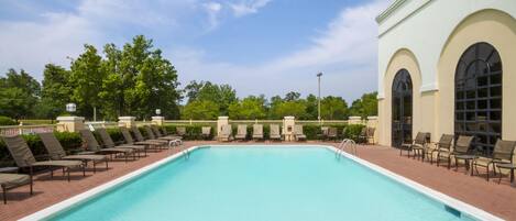 A rectangular swimming pool with a clear blue water surface, surrounded by lounge chairs and a building with arched windows.