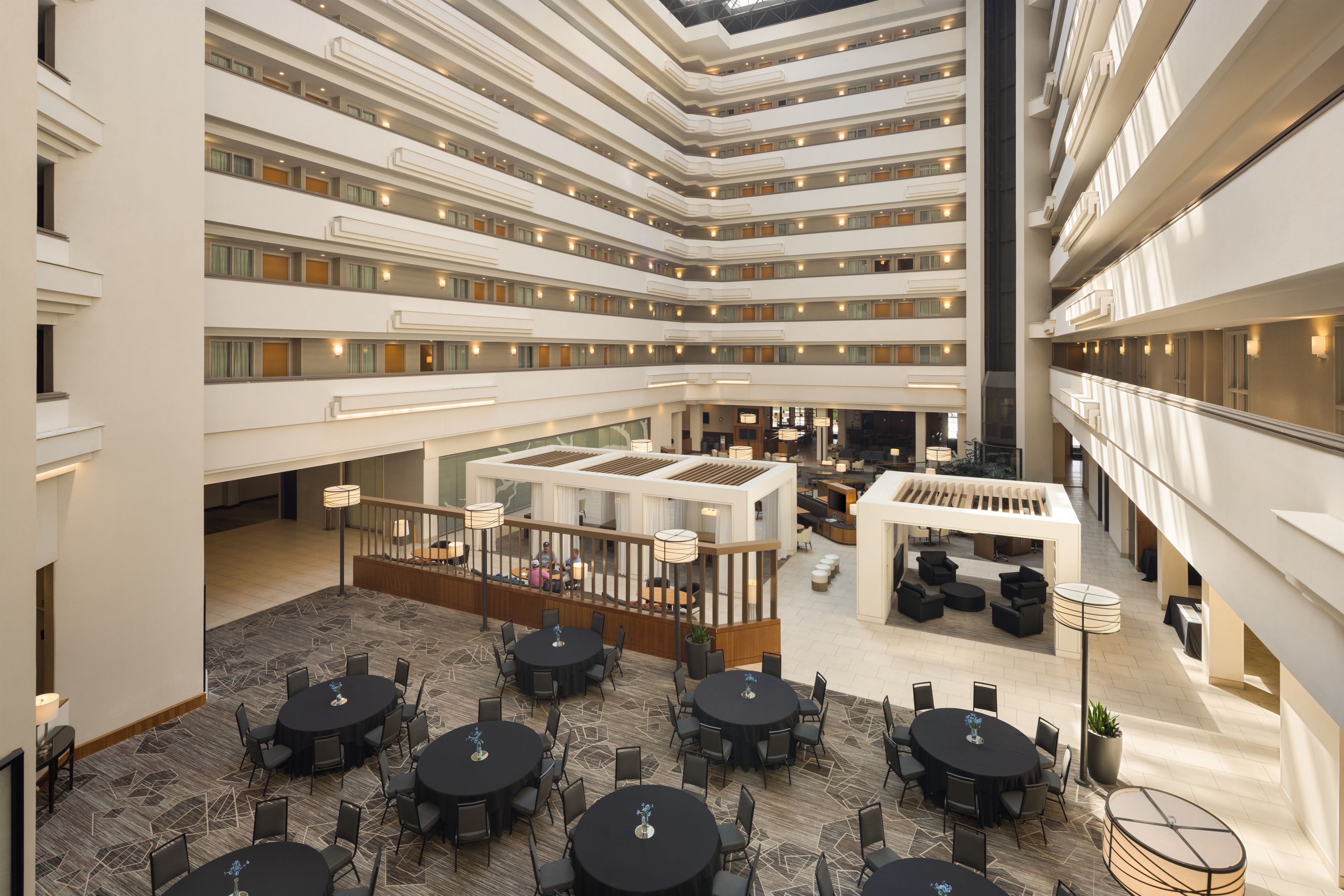 Un vestíbulo de hotel de varios niveles con un espacio central abierto, múltiples zonas de restauración y un diseño moderno.