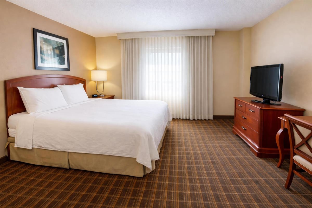 Une chambre d’hôtel avec un grand lit, une télévision, une commode et une fenêtre avec des rideaux.