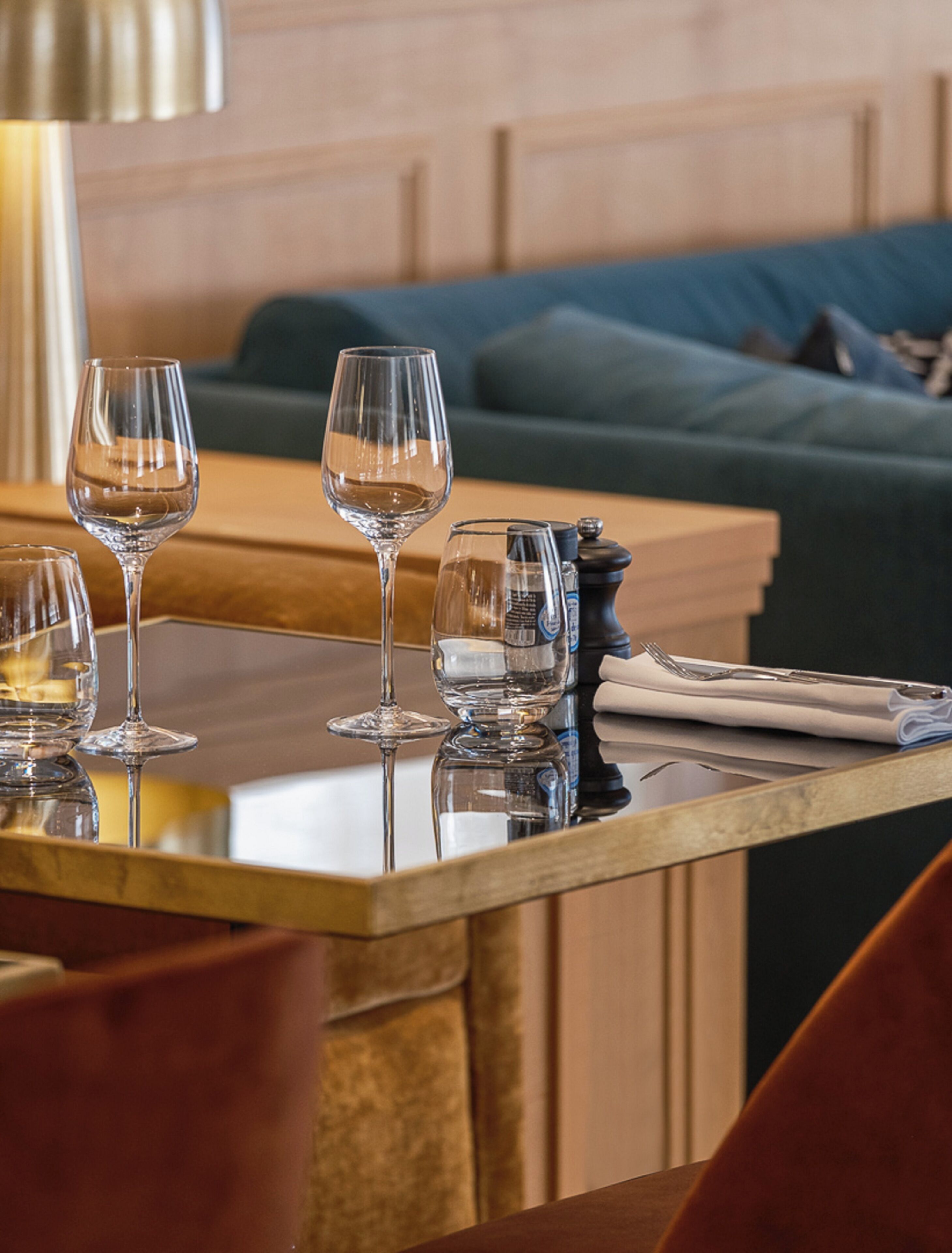 A dining table with wine glasses and a salt shaker, a folded napkin, and a spoon.