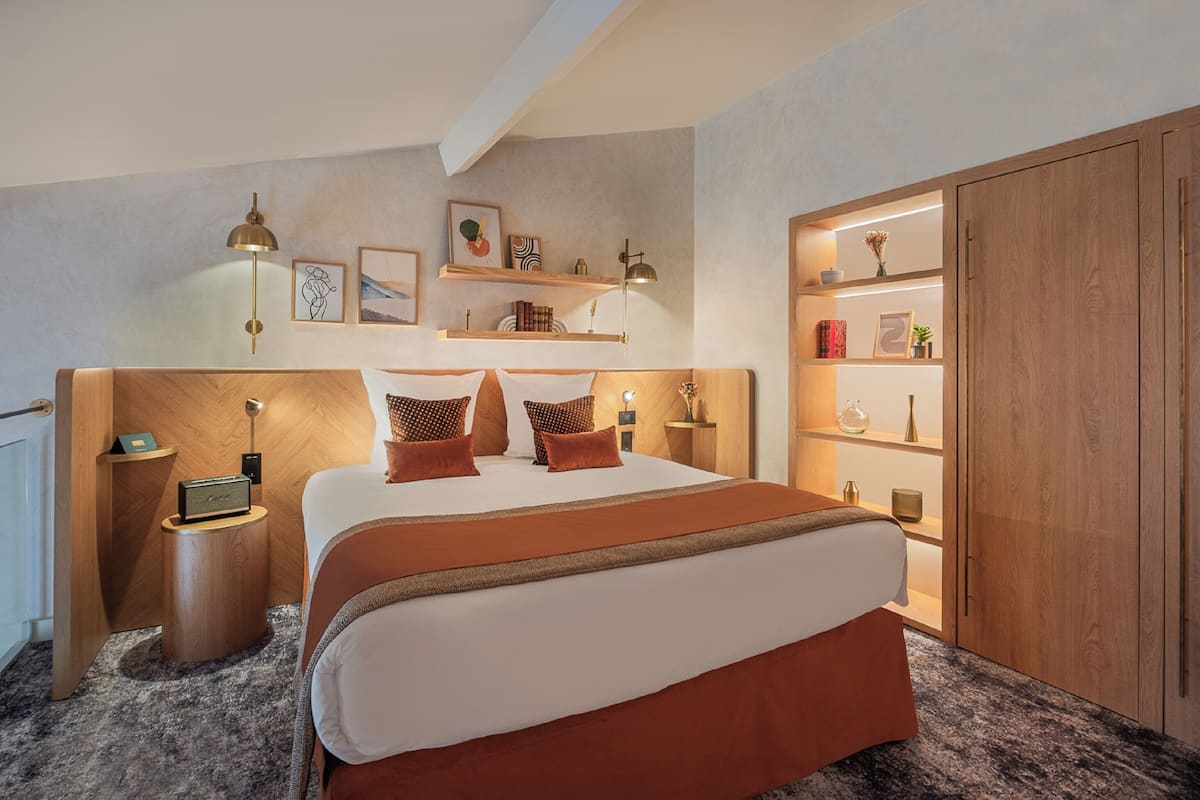 Ein modernes Hotelzimmer mit einem großen Bett, einem Holz-Kopfteil, Nachttischen und integrierten Regalen mit Dekoration.