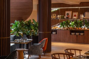 A restaurant interior with a wooden bar, seating area, and potted plants.