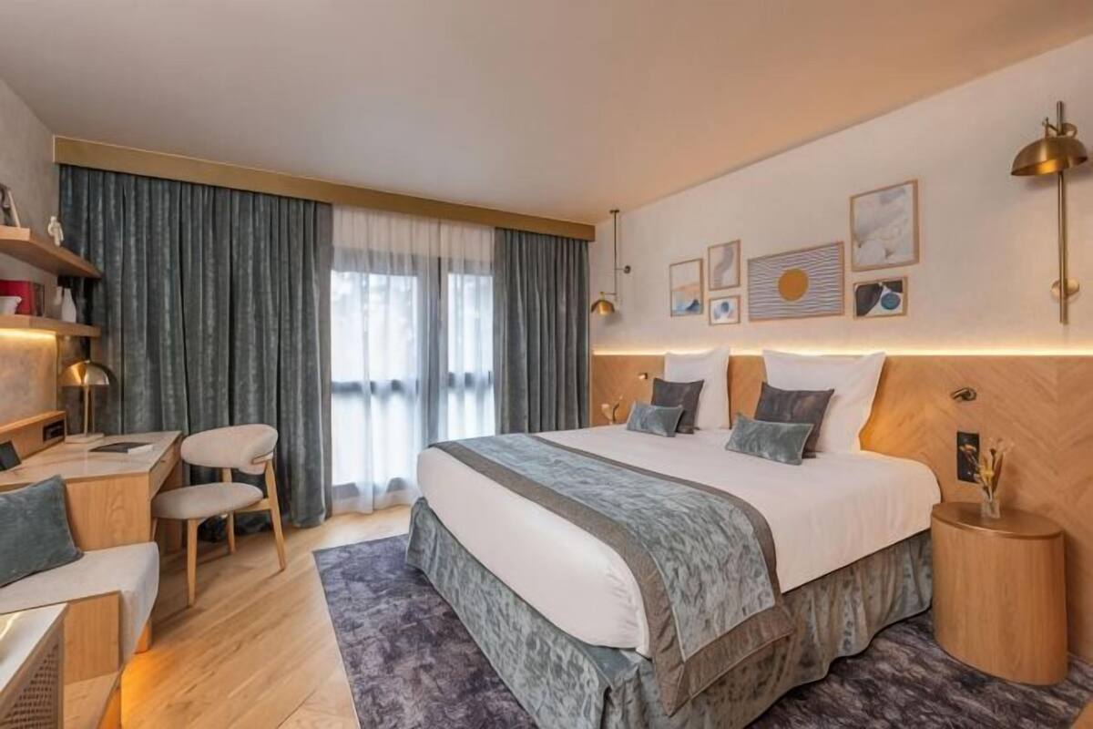 Ein Hotelzimmer mit einem großen Bett, einem Schreibtisch, einem Stuhl, einem Nachttisch und einem Fenster mit Vorhängen.