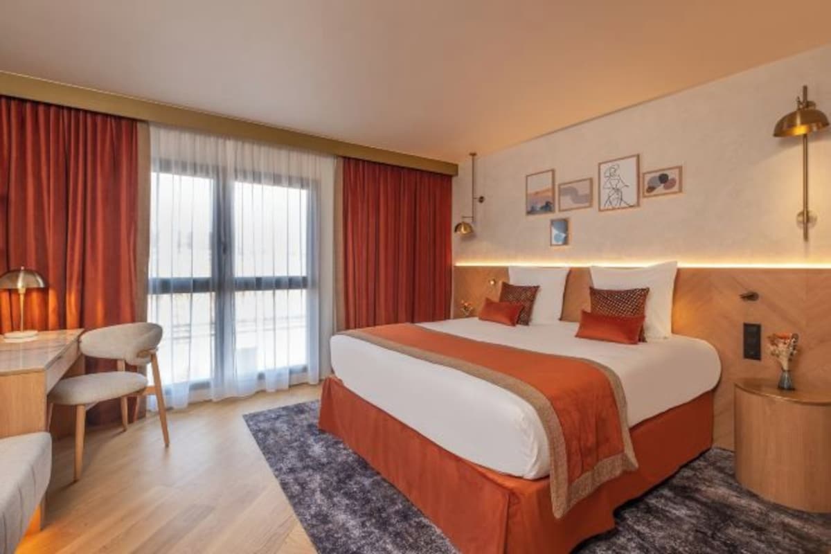 A hotel room with a large bed, a desk with a chair, and a window with curtains.
