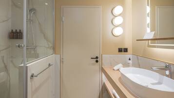 Un baño moderno con cabina de ducha de vidrio, un lavabo ovalado grande y un mueble de tocador con espejo.