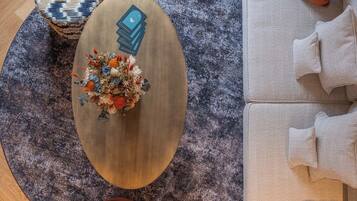 Una habitación con una mesa redonda de madera, una alfombra estampada, un sofá con cojines y un jarrón decorativo con flores.