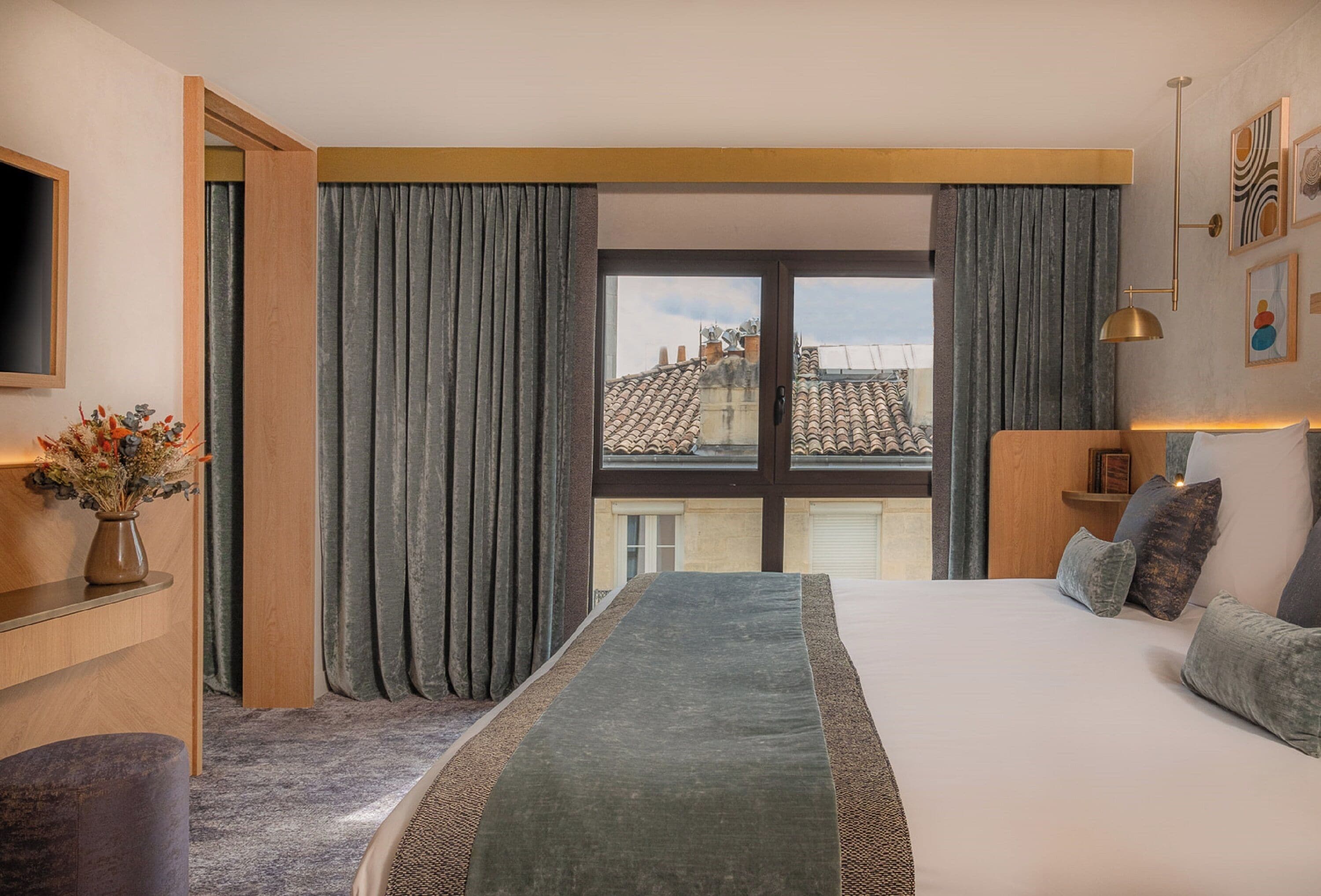 Habitación de hotel moderna con una cama grande, un escritorio y vistas de la ciudad a través de amplios ventanales.